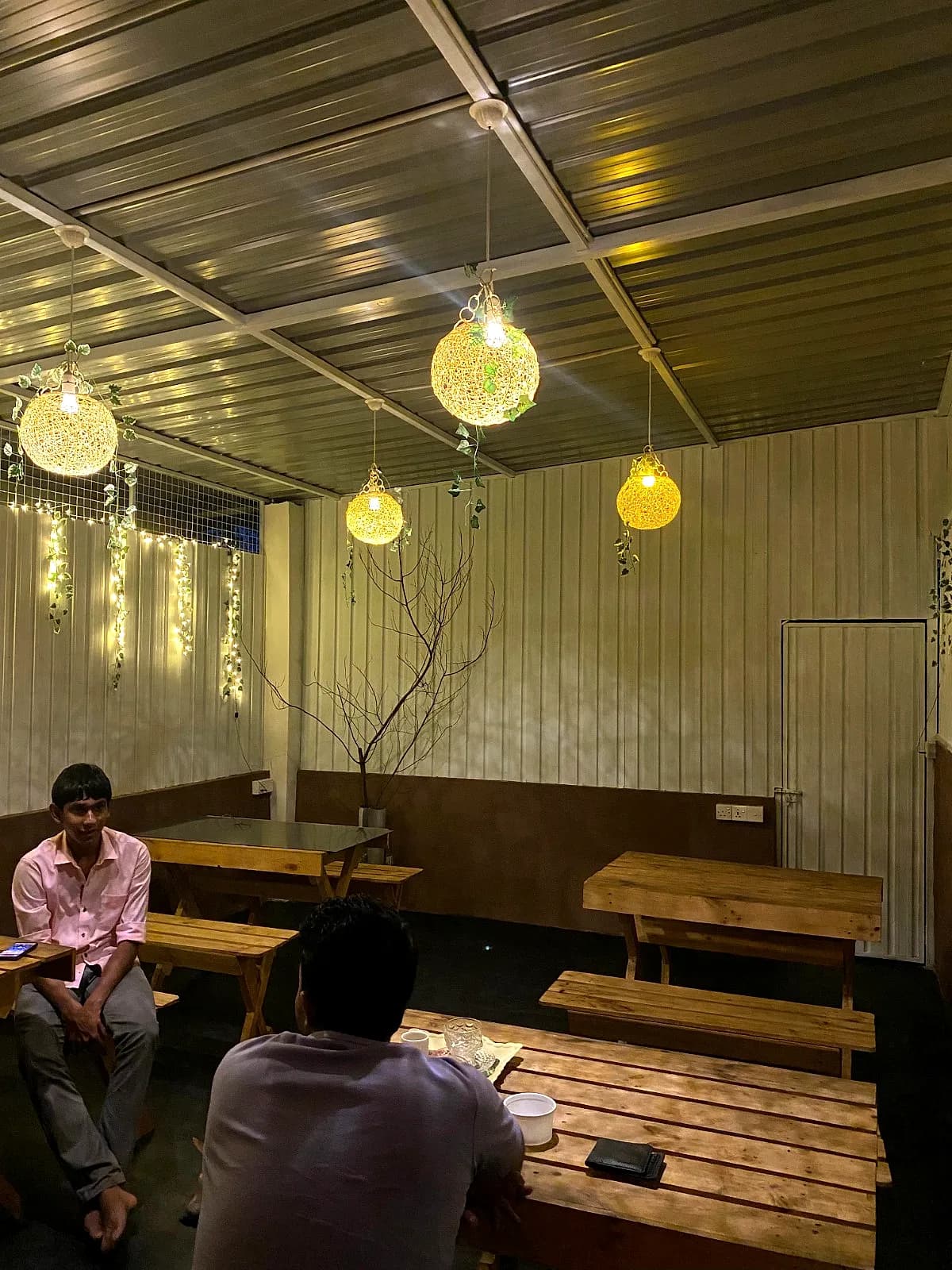 Covered dining deck under woven globe lanterns with wooden benches