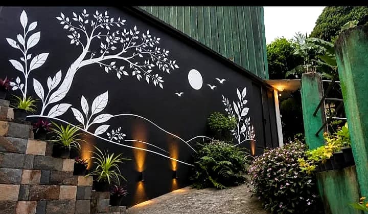 Hand-painted white tree mural on a black wall lit by warm garden lights