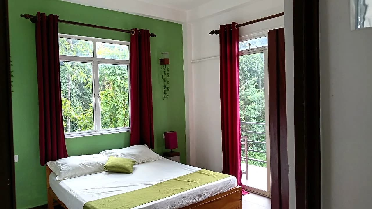 Bedroom with red drapes opening to a green jungle view and a small balcony